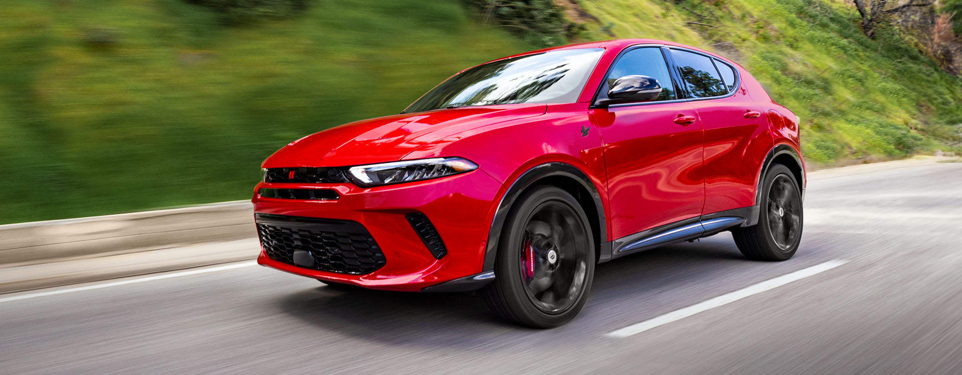 Un Dodge Hornet R/T PHEV 2025 rojo andando por una autopista con el fondo difuminado.