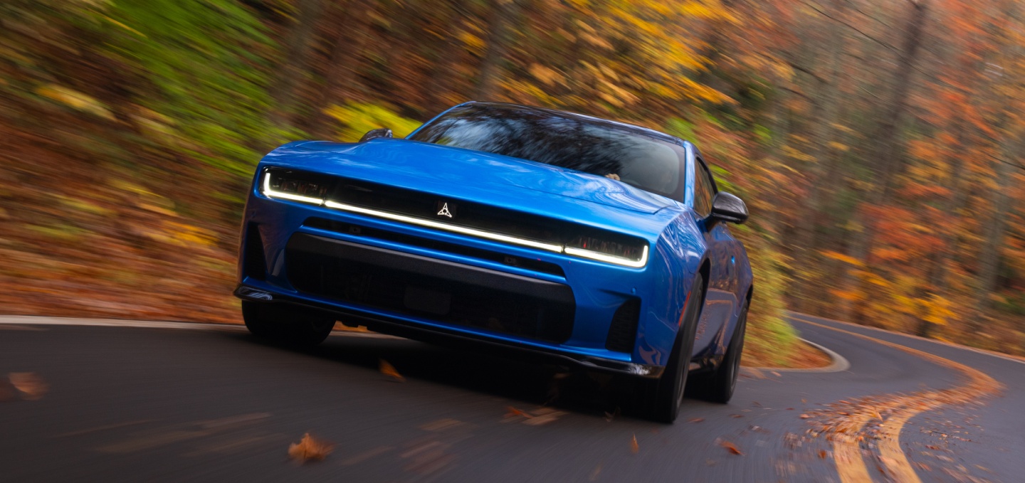 Un Dodge Charger Scat Pack 2027 azul tomando una curva en una carretera rural.