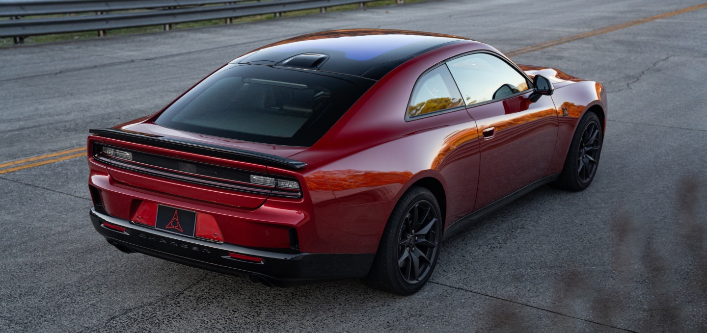 Un Dodge Charger Scat Pack 2027 rojo con techo negro, fotografiado de perfil trasero.