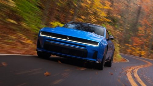 Un Dodge Charger Scat Pack 2027 azul tomando una curva en una carretera rural.
