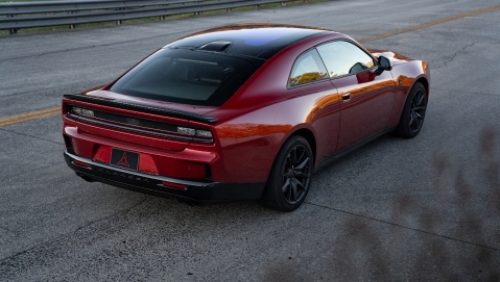 Un Dodge Charger Scat Pack 2027 rojo con techo negro, fotografiado de perfil trasero.