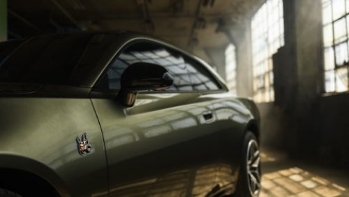El lado del conductor de un Dodge Charger Scat Pack 2027 verde oliva, estacionado en un garaje industrial.