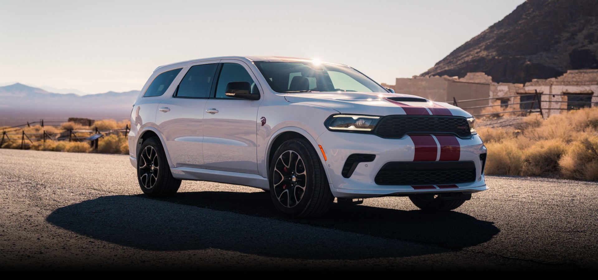 Un Dodge Durango SRT Hellcat Jailbreak 2027 blanco con dos franjas rojas centrales estacionado en una carretera en el desierto. Pura arrogancia.