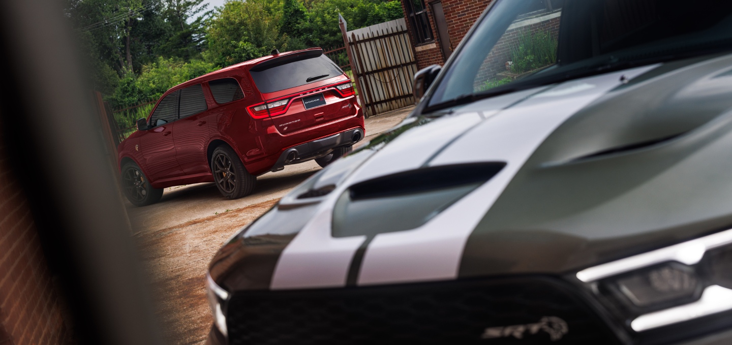 Dos modelos Dodge Durango 2027; en primer plano, la parte delantera de un Durango SRT Hellcat Jailbreak gris con dos franjas centrales blancas, y al fondo, un Durango SRT Hellcat Jailbreak rojo.
