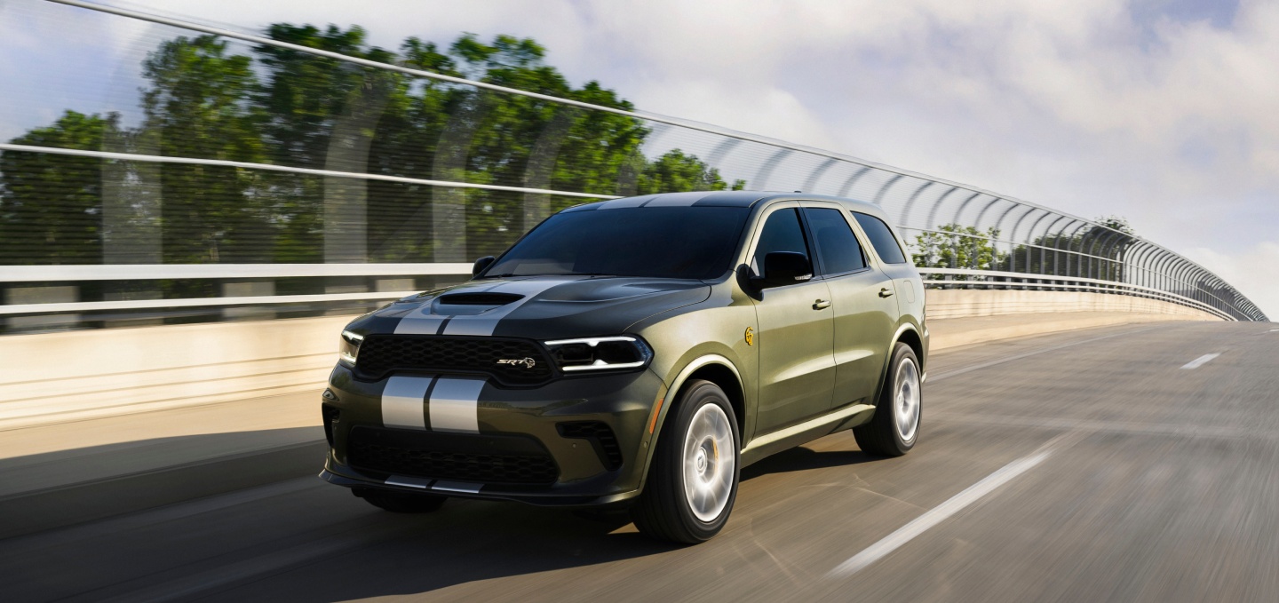 Un Dodge Durango SRT Hellcat Jailbreak​​​​​​​ 2027 en verde oliva con dos franjas centrales blancas andando por un puente de una autopista.