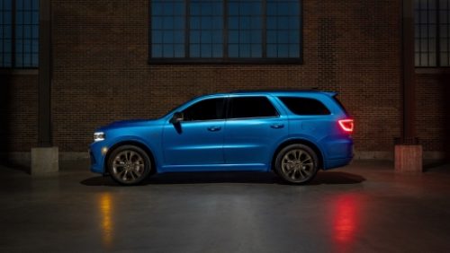 Perfil de un Dodge Durango R/T 392 2027 azul estacionado al lado de un edificio de ladrillo.