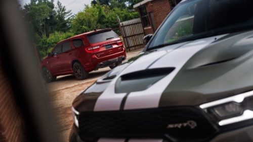 Dos modelos Dodge Durango 2027; en primer plano, la parte delantera de un Durango SRT Hellcat Jailbreak gris con dos franjas centrales blancas, y al fondo, un Durango SRT Hellcat Jailbreak rojo.