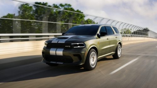 Un Dodge Durango SRT Hellcat Jailbreak​​​​​​​ 2027 en verde oliva con dos franjas centrales blancas andando por un puente de una autopista.