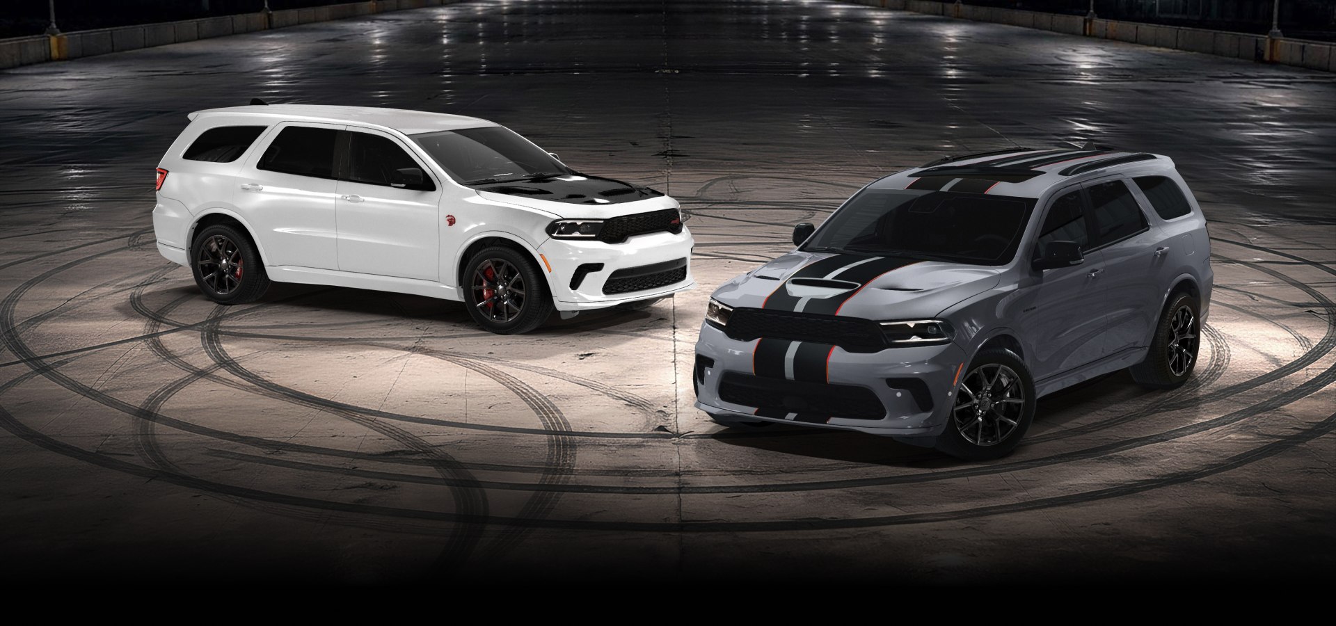Un Dodge Durango SRT Hellcat Jailbreak 2027 blanco con un inserto negro en el capó y un Dodge Durango GT Hemi V8 2027 gris con dos franjas centrales negras y rojas, estacionados en perpendicular uno frente al otro en un lugar vacío por la noche. Inteligente y sin complicaciones.