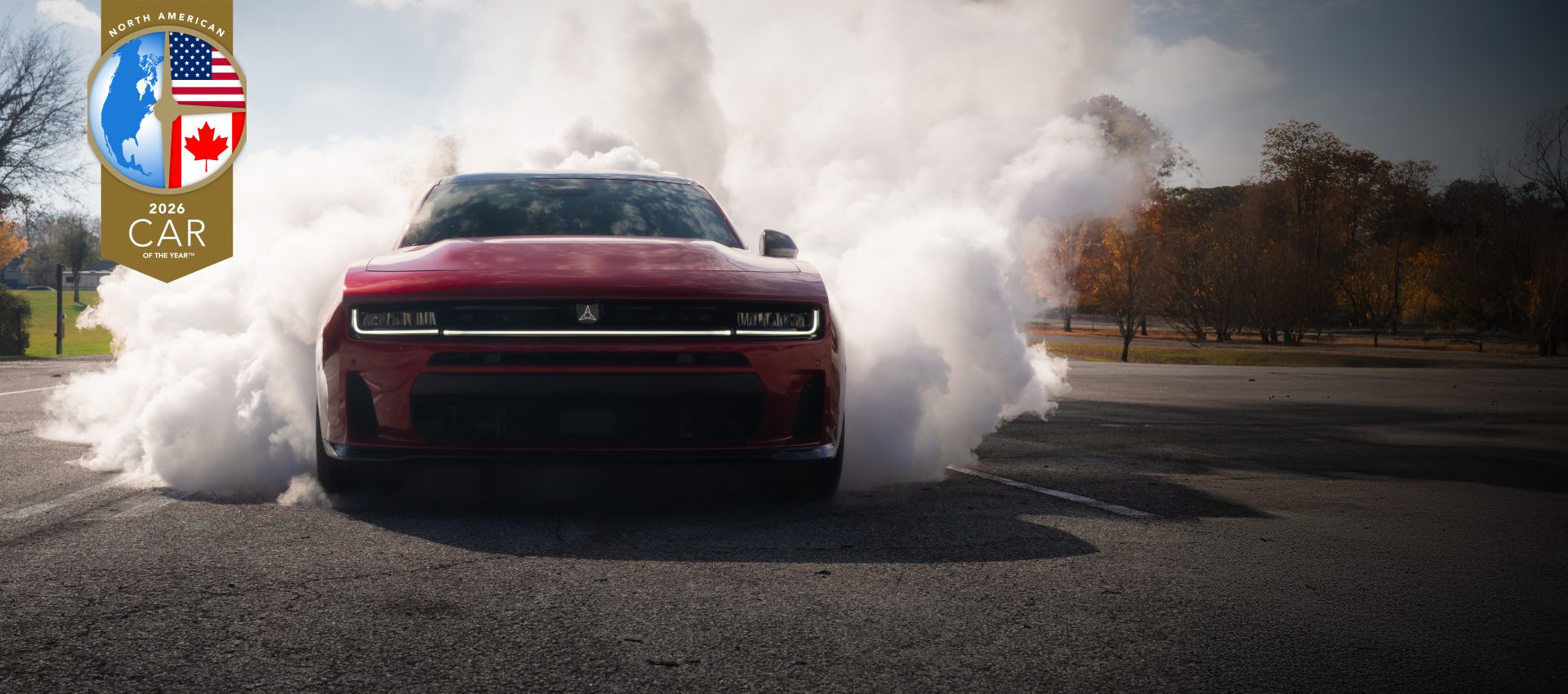 Ángulo del extremo delantero de un Dodge Charger Scat Pack 2026 en el asfalto, con humo blanco que ondula desde la parte trasera del vehículo. North American 2026 Car of the Year.