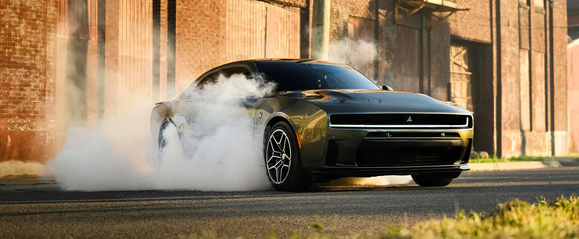 Un Dodge Charger Scat Pack 2026 verde de dos puertas haciendo un derrape, detenido y con humo saliendo de sus neumáticos traseros.