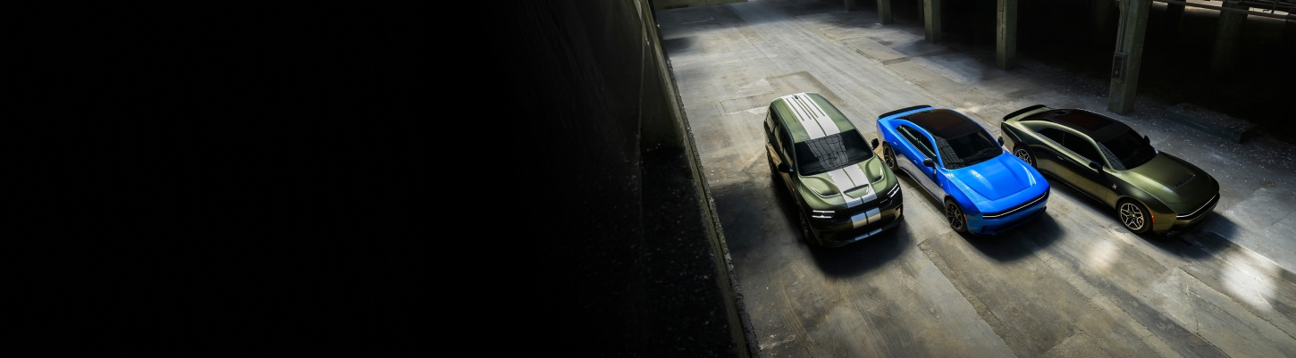 Una toma aérea de un Dodge Durango SRT Hellcat Jailbreak 2026 verde con dos franjas centrales blancas, un Dodge Charger Scat Pack 2026 azul con techo negro y un Dodge Charger Scat Pack Plus 2026 verde estacionados uno junto al otro.
